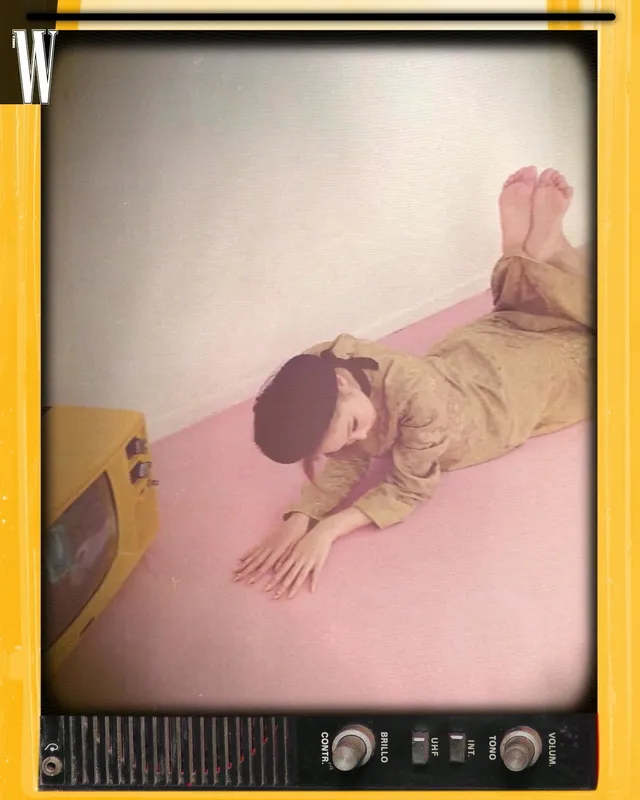 Jennie Kim lying barefoot on a pink studio floor in a photograph framed by a television.