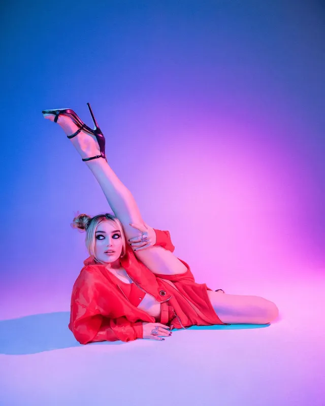 Meg Donnelly reclining in a red outfit with one leg raised in black heels.