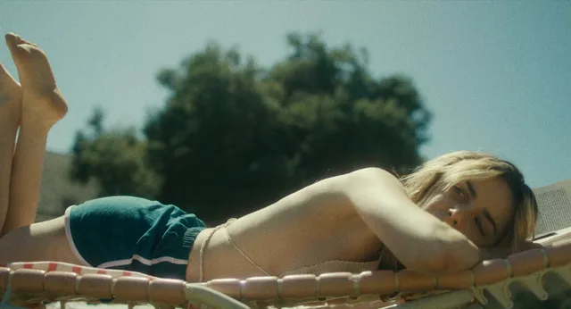 Kiernan Shipka reclining barefoot on a sun lounger in a film scene.