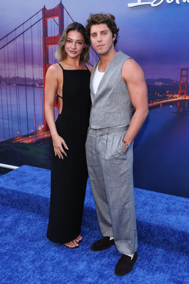 Madelyn Cline posing beside a man in a long black dress and heels.