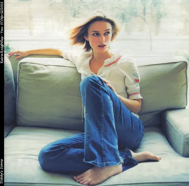 Keira Knightley seated on a pale green sofa in jeans and a light blouse.