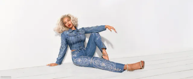 Beyoncé sitting barefoot in a denim outfit against a white backdrop.