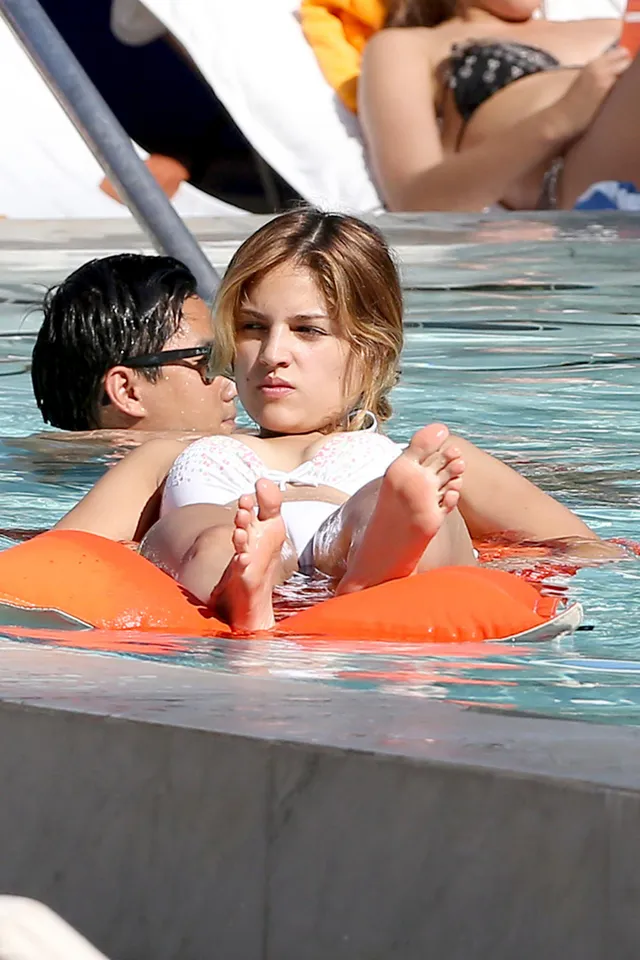Eiza González relaxing in a pool with bare soles raised.