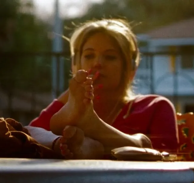Ashley Benson resting her bare feet on a table during a screen scene.