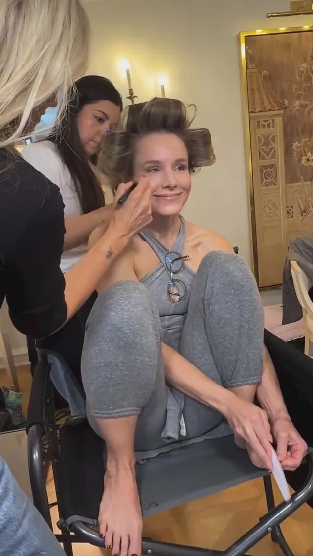 Kristen Bell having makeup applied while seated barefoot.