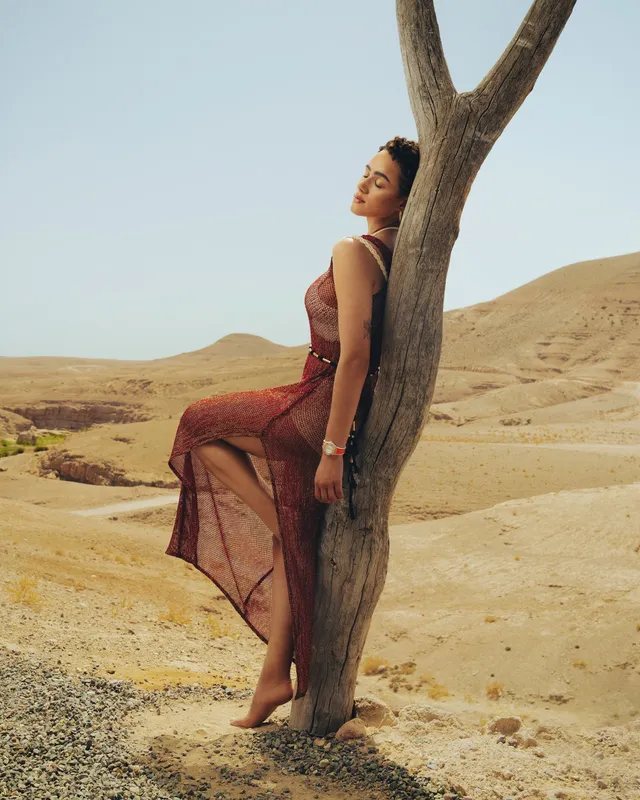 Nathalie Emmanuel leaning against a tree in a long red dress.
