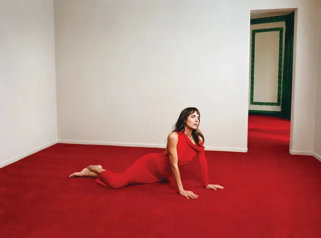 Dakota Johnson posing barefoot in a red dress on a red carpet.