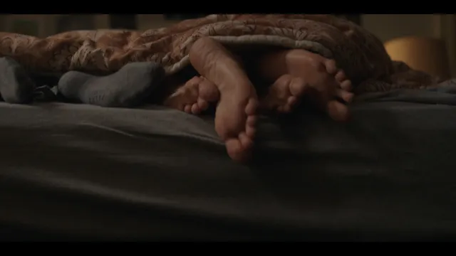 Whitney Peak shown in a close-up of bare feet on a bed in a scene.