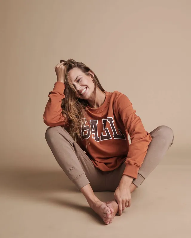 Josephine Skriver sitting cross-legged and barefoot in an orange sweatshirt and trousers.