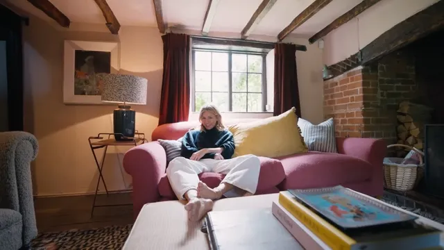 Sienna Miller sitting in a furnished room in a screen scene.