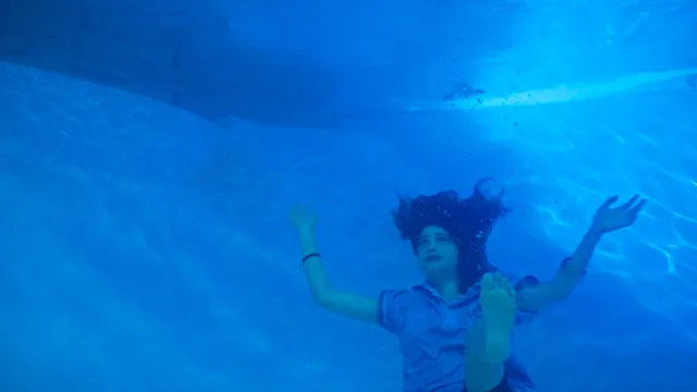 Odessa A'zion swimming underwater in a blue-lit scene.
