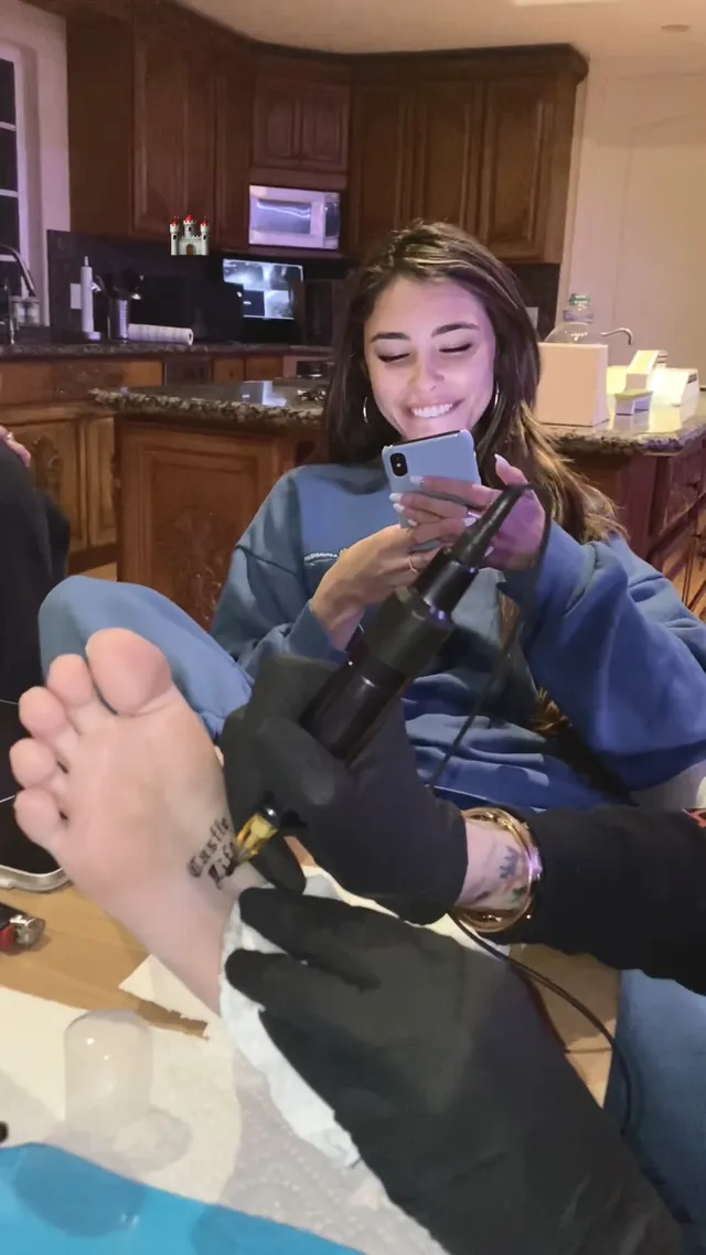 Madison Beer: seated indoors while a bare sole is being tattooed.
