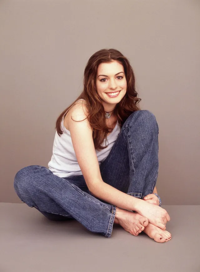 Anne Hathaway sitting barefoot in jeans for a studio portrait.