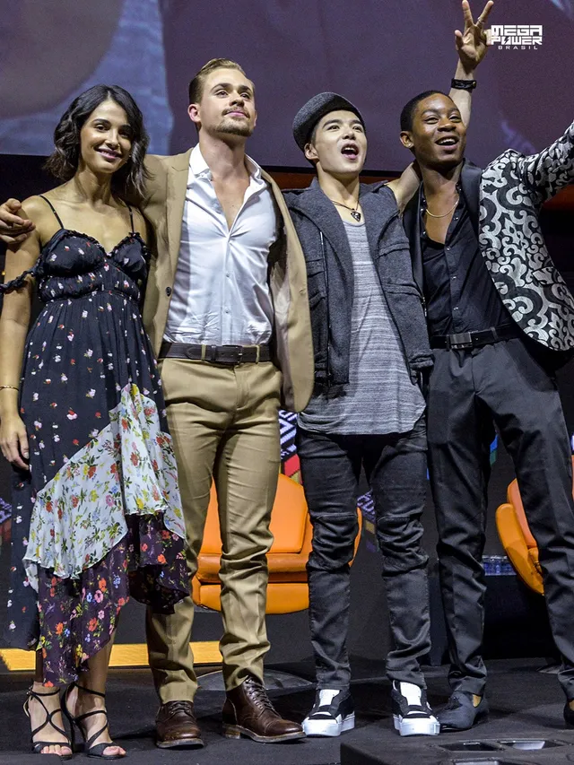 Naomi Scott posing with guests in a long patterned dress and heels.