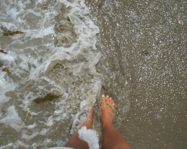 Demi Lovato standing barefoot at the edge of the sea.
