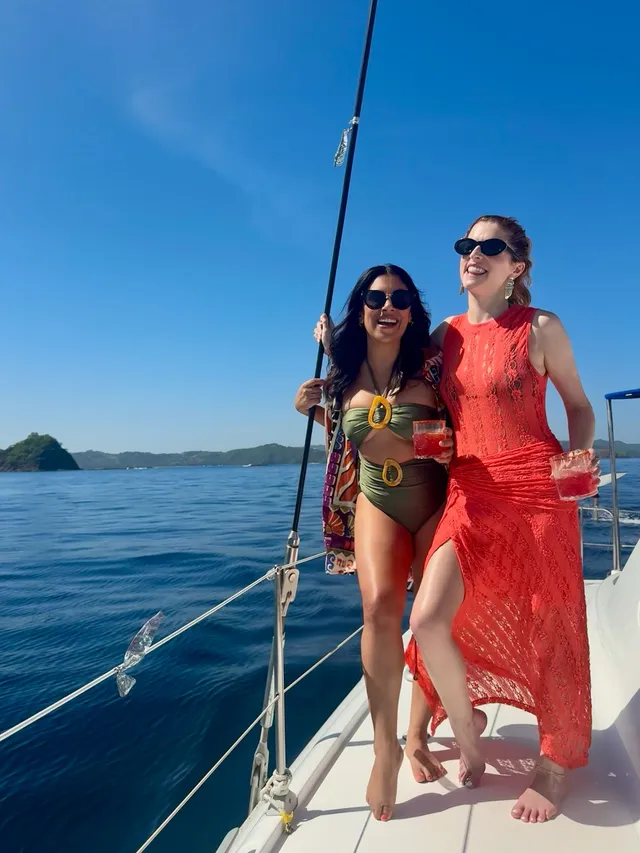 Anna Kendrick posing barefoot with a friend aboard a sailing boat.