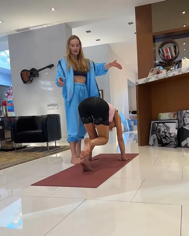 Kate Beckinsale stretching barefoot beside another person indoors.