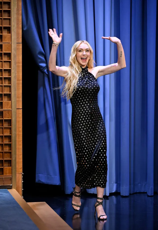 Lindsay Lohan standing onstage in a black dress and heels.