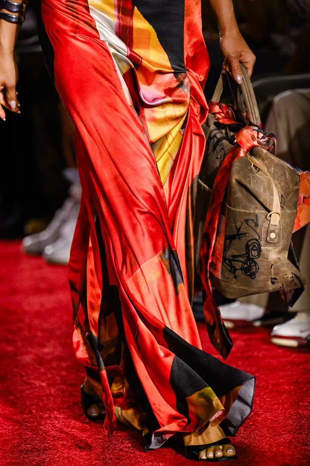 Shay Mitchell walking on a red carpet in a flowing patterned outfit.