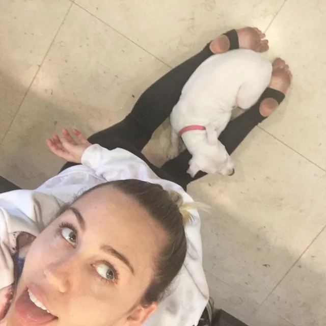 Miley Cyrus taking a selfie beside a dog.