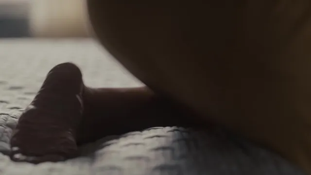 Elizabeth Olsen resting barefoot on a bed in a screen scene.