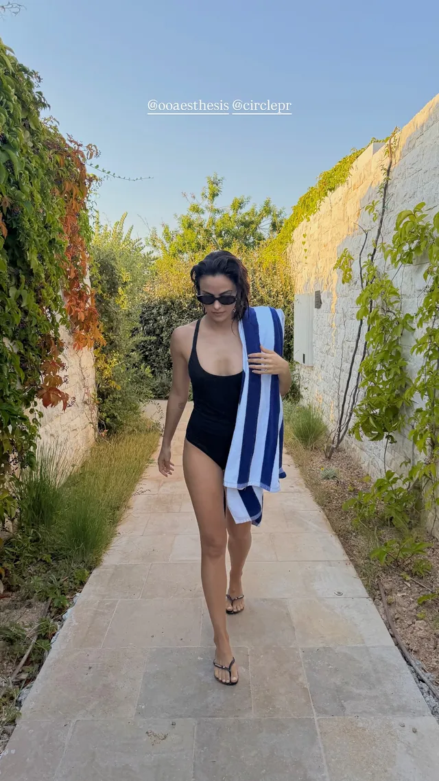 Camila Mendes walking along a stone path in a swimsuit and sandals.
