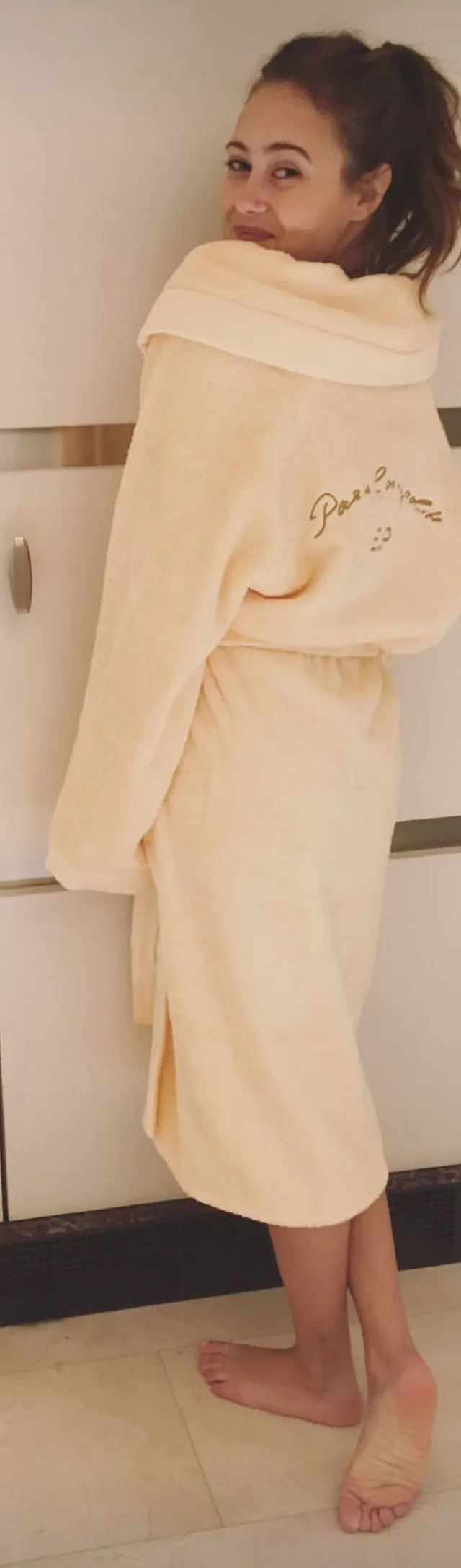 Ella Purnell looking back in a pale robe indoors.