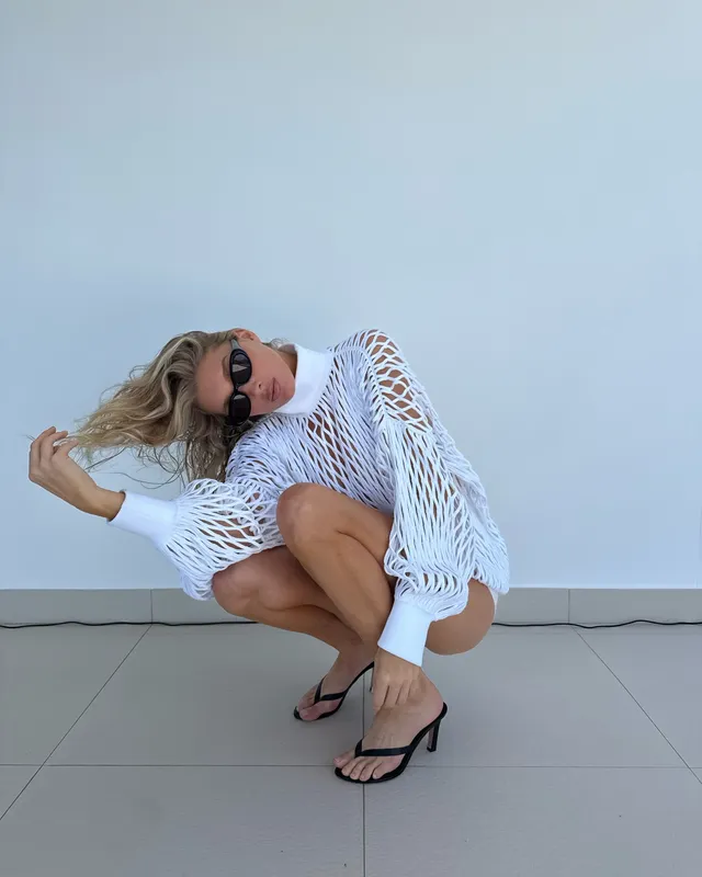 Elsa Hosk crouching in a white open-knit cover-up and black heeled sandals.