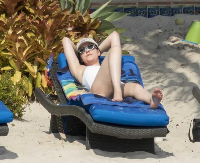 Dakota Johnson relaxing on a blue lounger with bare soles visible.
