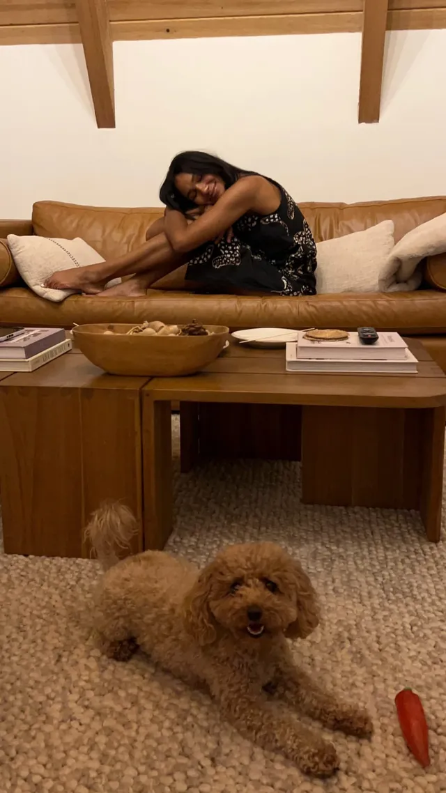 Greta Onieogou sitting barefoot on a sofa near a dog.
