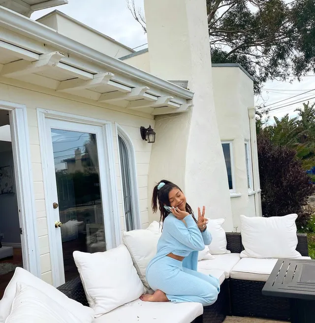 Sierra Capri sitting barefoot on an outdoor sofa in a blue outfit.