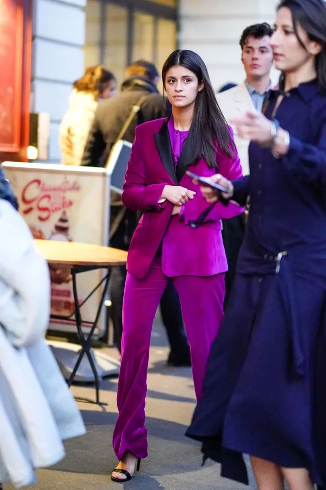 Anya Chalotra walking outdoors in a purple suit and black heels.