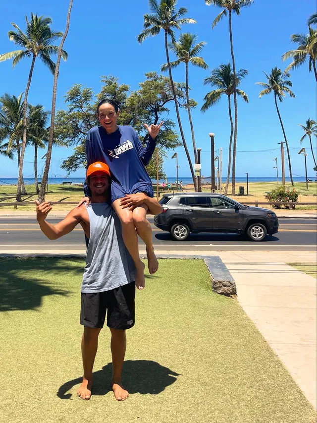 Chase Sui Wonders sitting barefoot on a companion's shoulders outdoors.