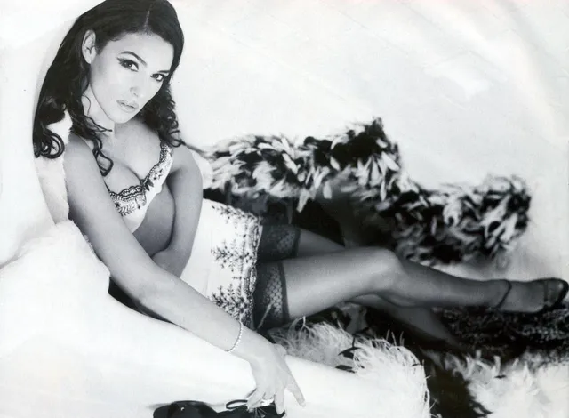 Monica Bellucci reclining on white bedding in stockings for a monochrome portrait.