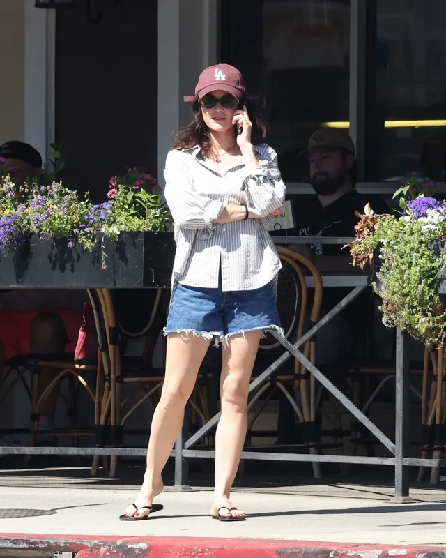 Lucy Hale standing on a pavement in denim shorts and a cap.