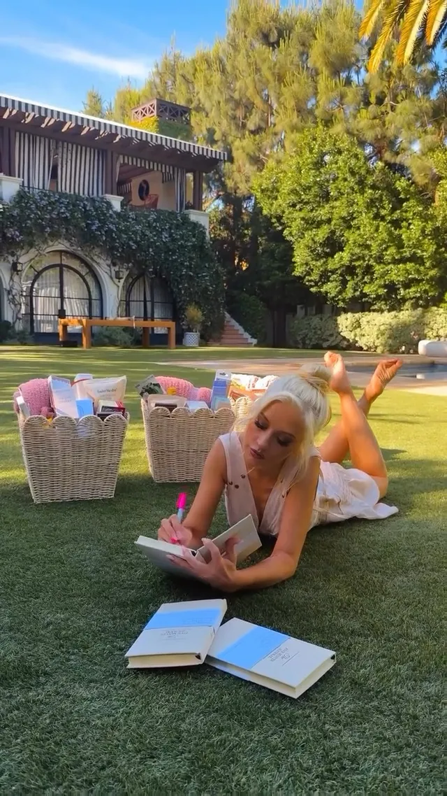 Christina Aguilera lying on grass beside open books with her bare soles raised.