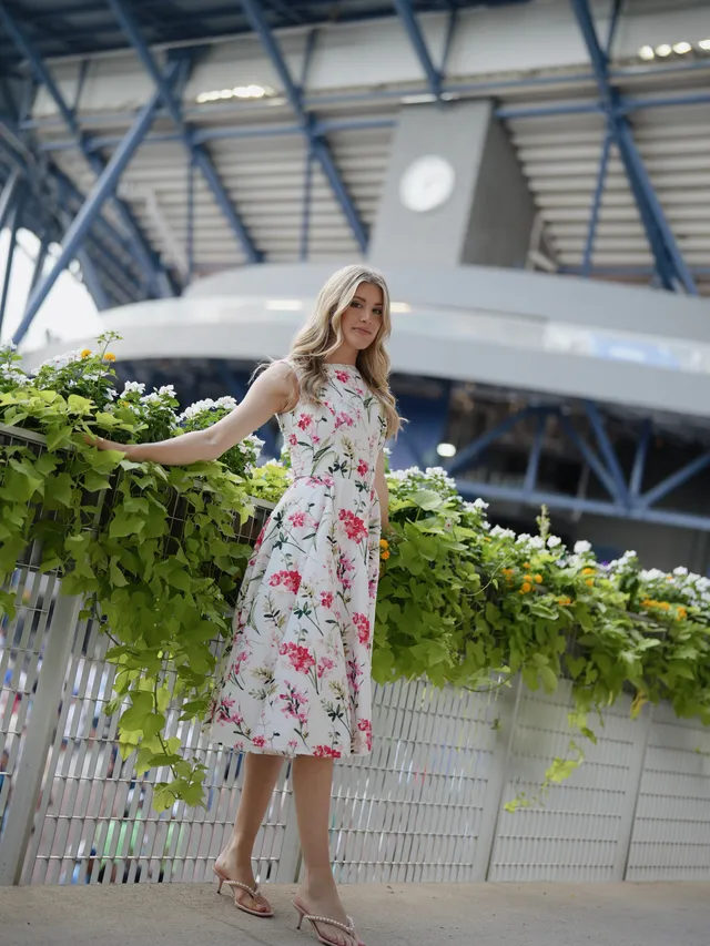Eugenie Bouchard standing on a terrace in heeled sandals and a long floral dress.