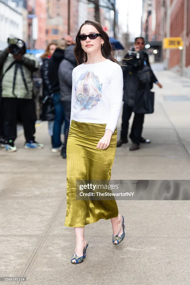 Victoria Pedretti walking outdoors in a green skirt and patterned heels.