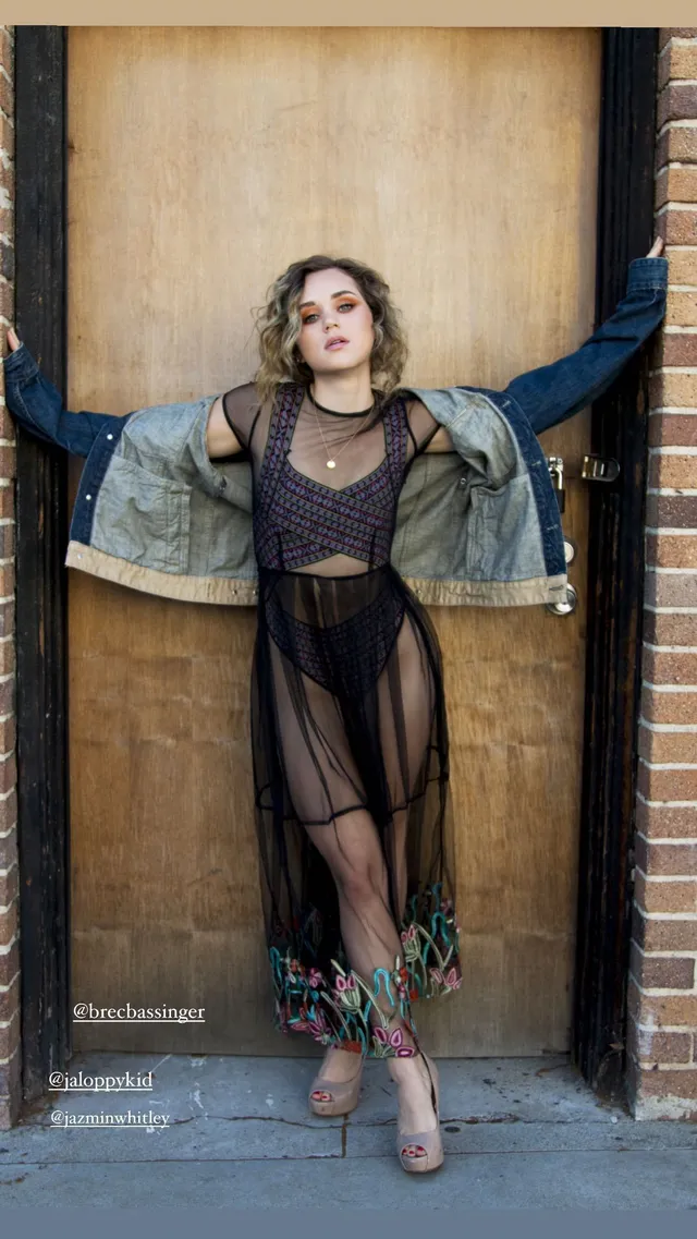 Brec Bassinger posing in a sheer dark outfit, denim jacket and patterned ankle boots.