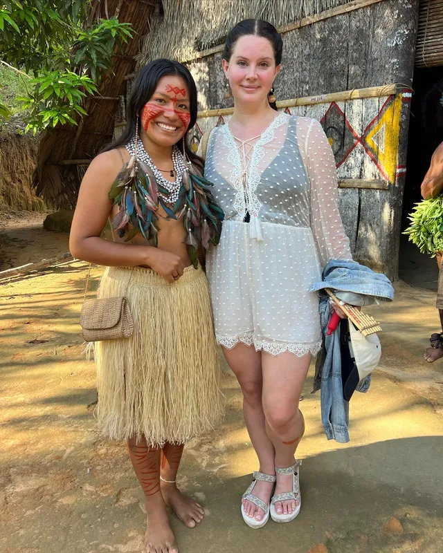 Lana Del Rey standing beside another person in a pale outfit and white flat sandals.