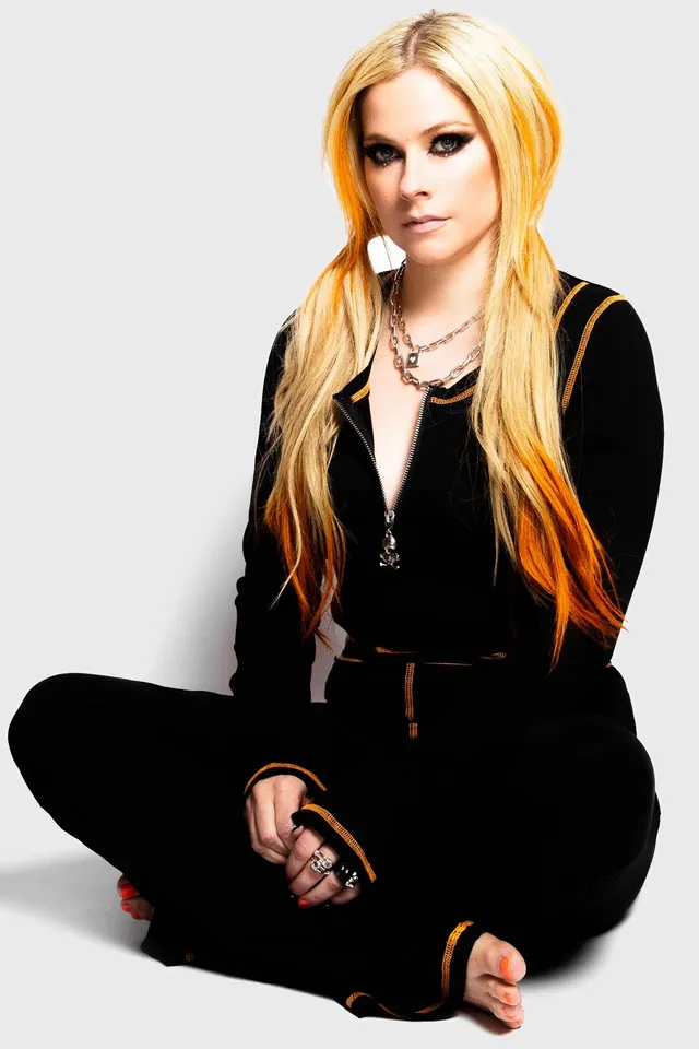 Avril Lavigne sitting cross-legged in a black outfit with a bare sole visible.