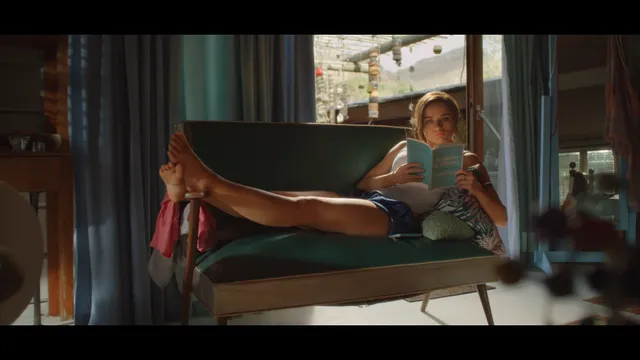 Joey King reclining barefoot in an armchair in a film scene.