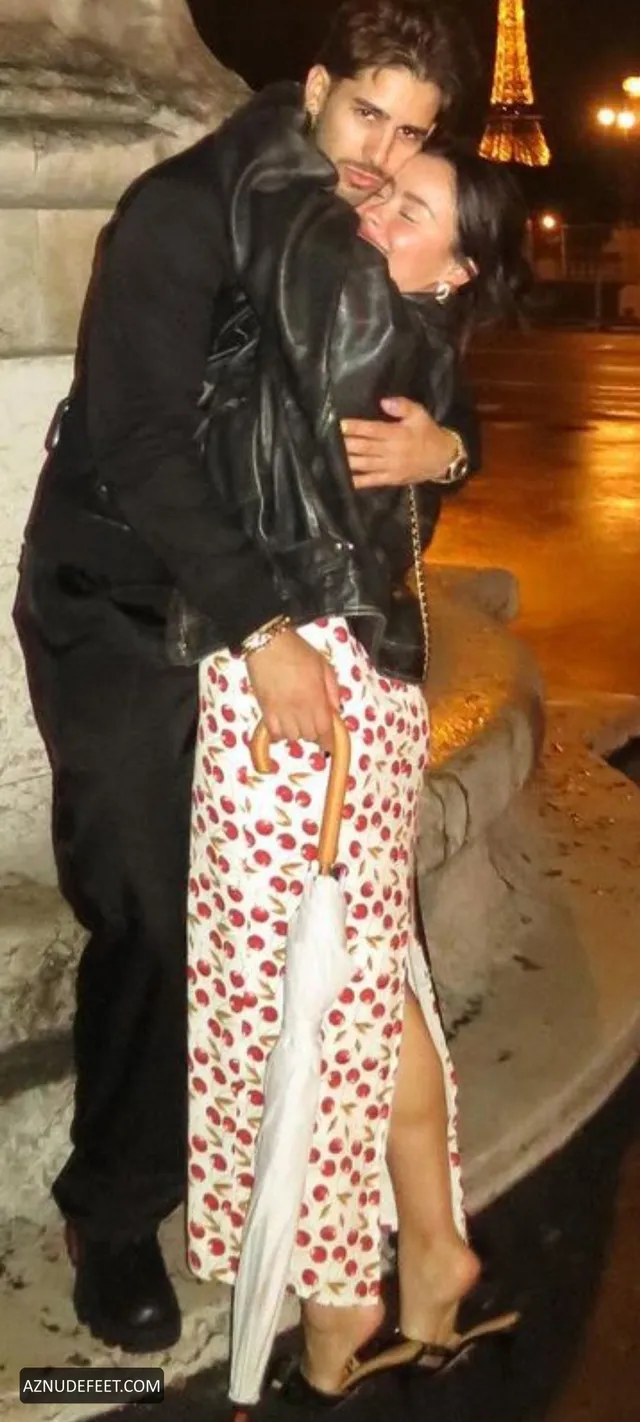 Cierra Ramirez in a patterned skirt and heeled sandals embracing her partner at night.