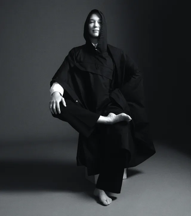 Léa Seydoux sitting in a monochrome studio portrait in a dark outfit.