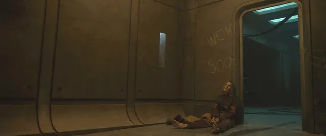 Rebecca Ferguson sitting on a kitchen floor in a dark film scene with bare feet extended.