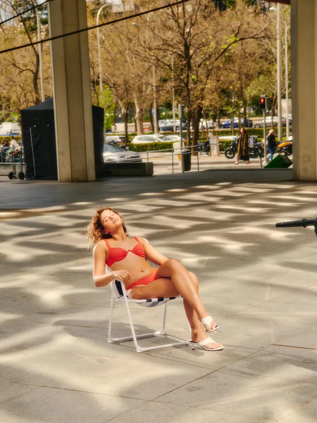 Nicole Wallace reclining on an outdoor chair in a red outfit and white heels.