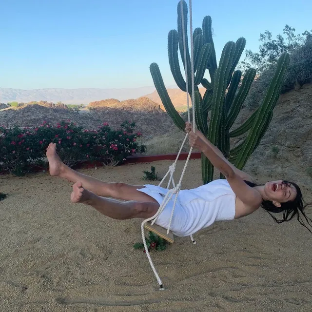 Phoebe Tonkin sitting on a swing in a desert garden.