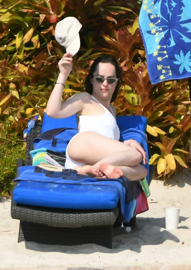 Dakota Johnson reclining on a blue lounger with bare soles visible.