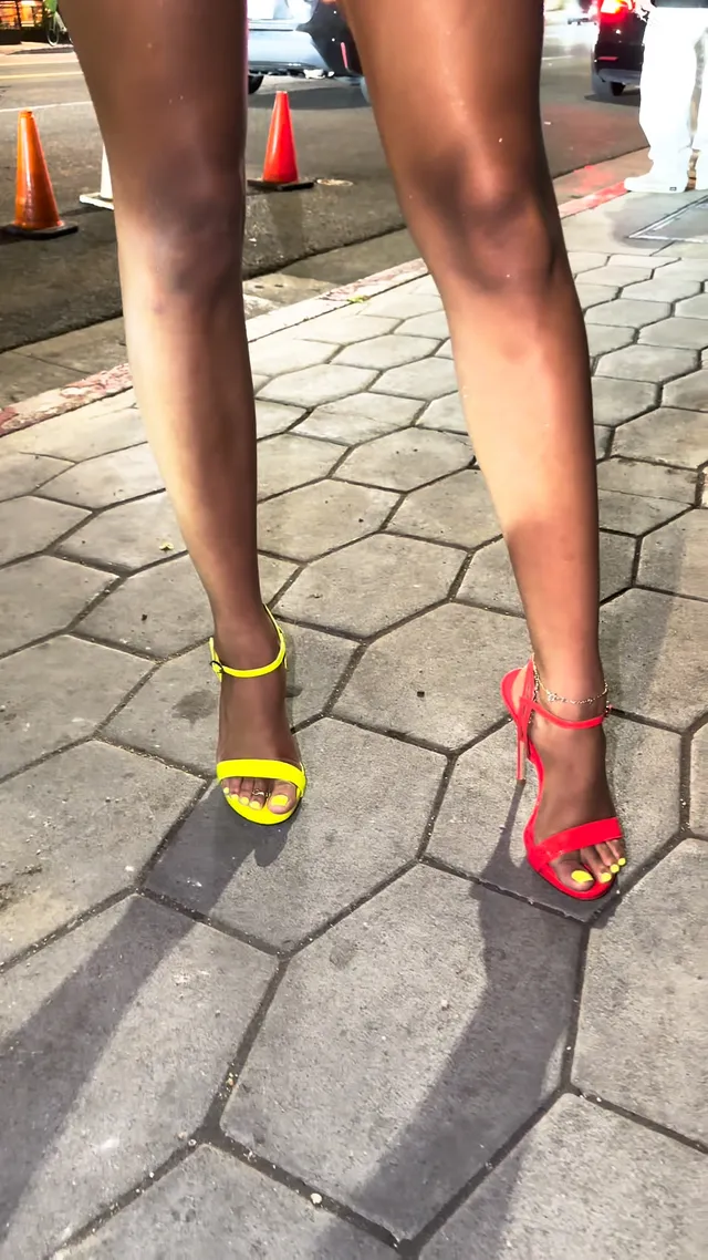 Tyla showing mismatched bright heeled sandals on a paved surface.