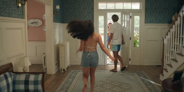 Lola Tung standing barefoot in shorts during a scene.